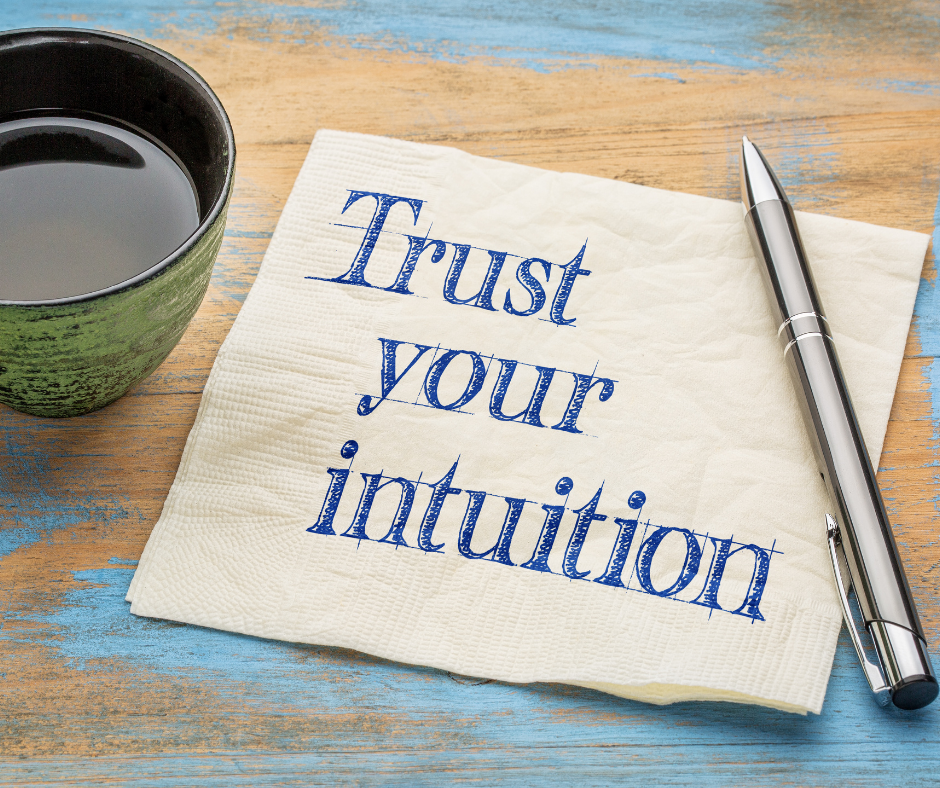 White paper napkin on table with tea cup and pen. On the napkin is sketched, "Trust your intuition."