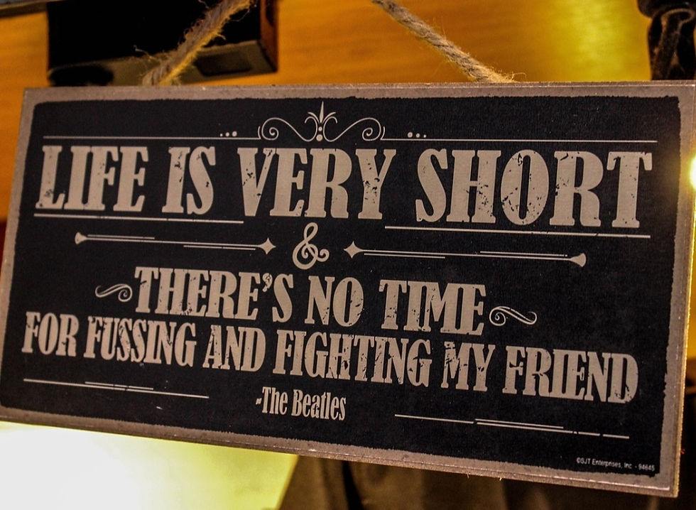 Sign with white text on black reading "Life is very short & there's no time for fussing and fighting my friend - The Beatles." Cozy setting.