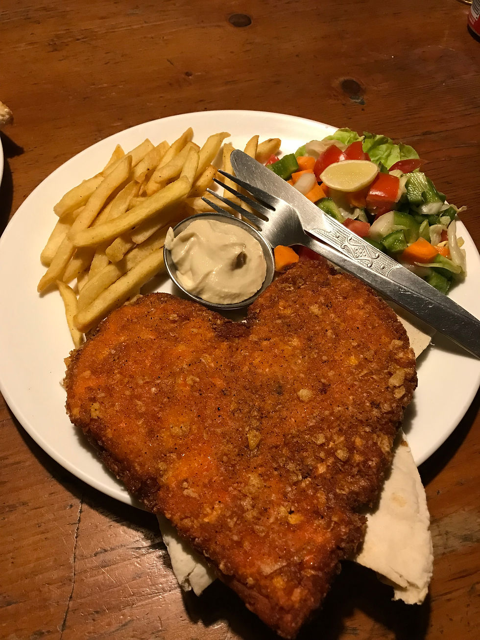 A heart shaped chicken schnitzel with chips and salad