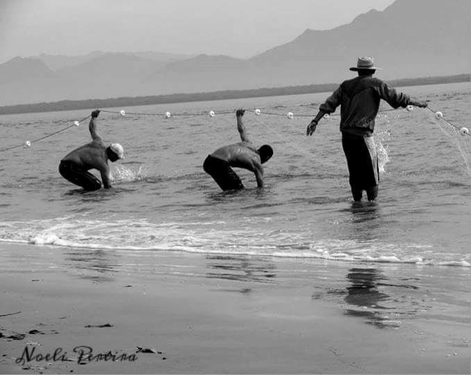 A imagem mostra três pescadores manuseando uma rede de pesca no mar.