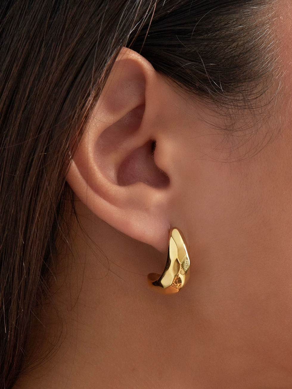 Detailansicht der goldenen Lana Ohrringe am Ohr getragen – modernes organisches Design mit strukturiertem Finish.