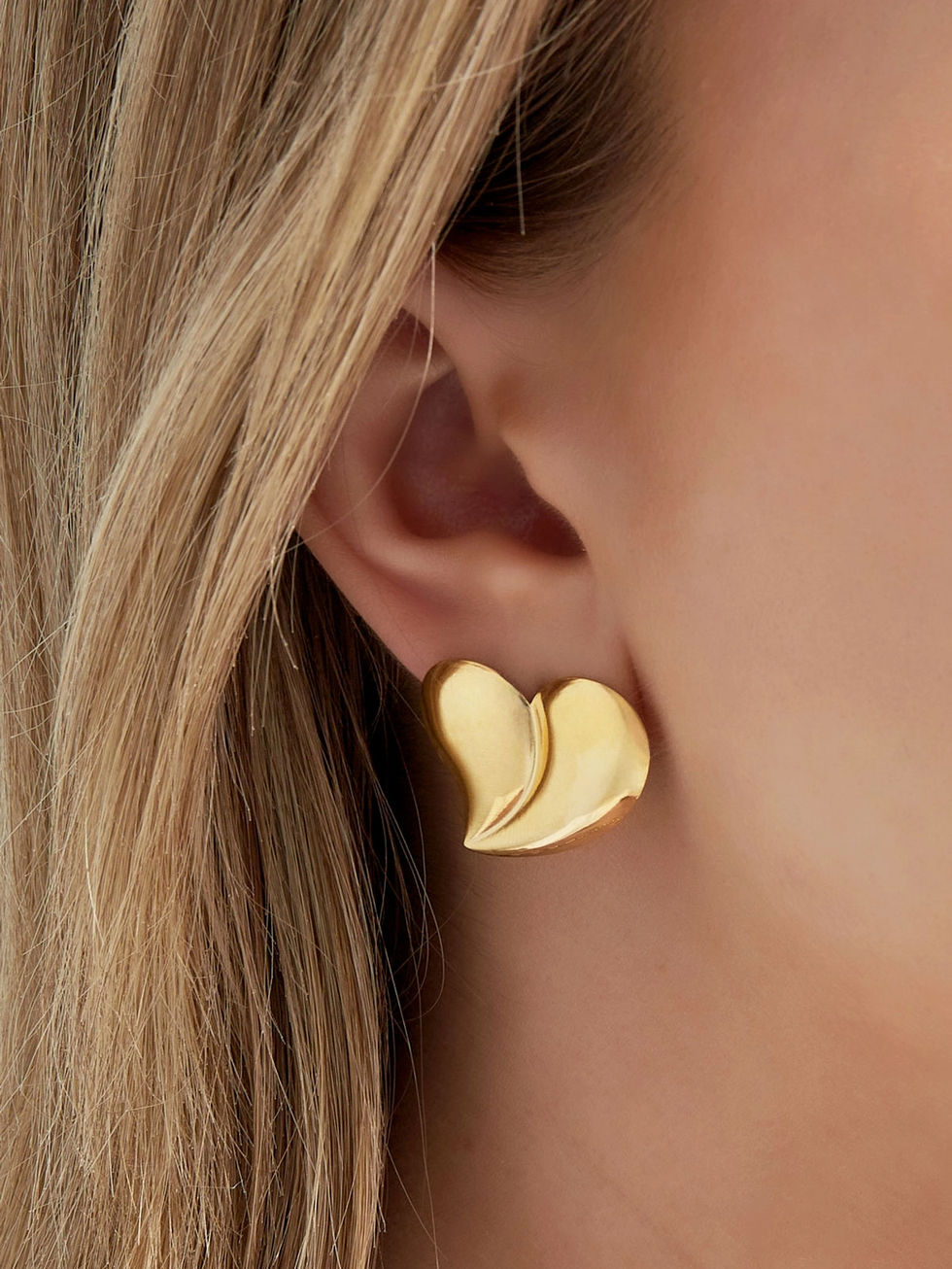 Detailansicht der goldenen Juliana Herz-Ohrringe am Ohr getragen – modernes skulpturales Design für elegante Looks.
