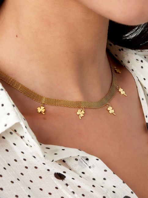 Die goldene Eloise Mesh-Kette mit Kleeblatt-Anhängern getragen zu einer gepunkteten Bluse – moderner Glücksbringer-Schmuck.