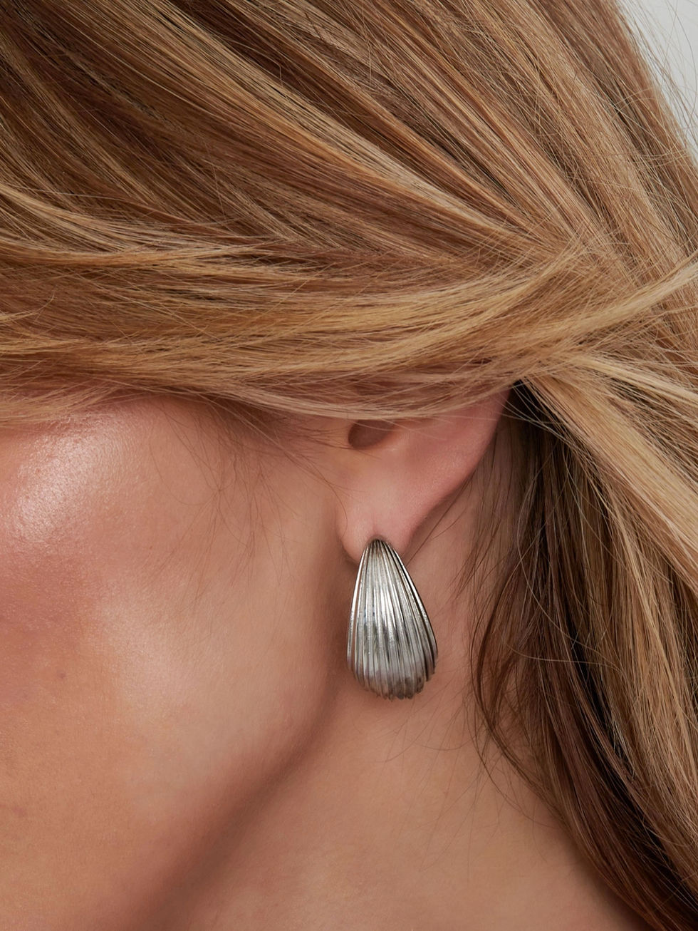 Die silberne Variante der Eldoria Ohrringe am Ohr – moderner, skulpturaler Schmuck für stilbewusste Looks.