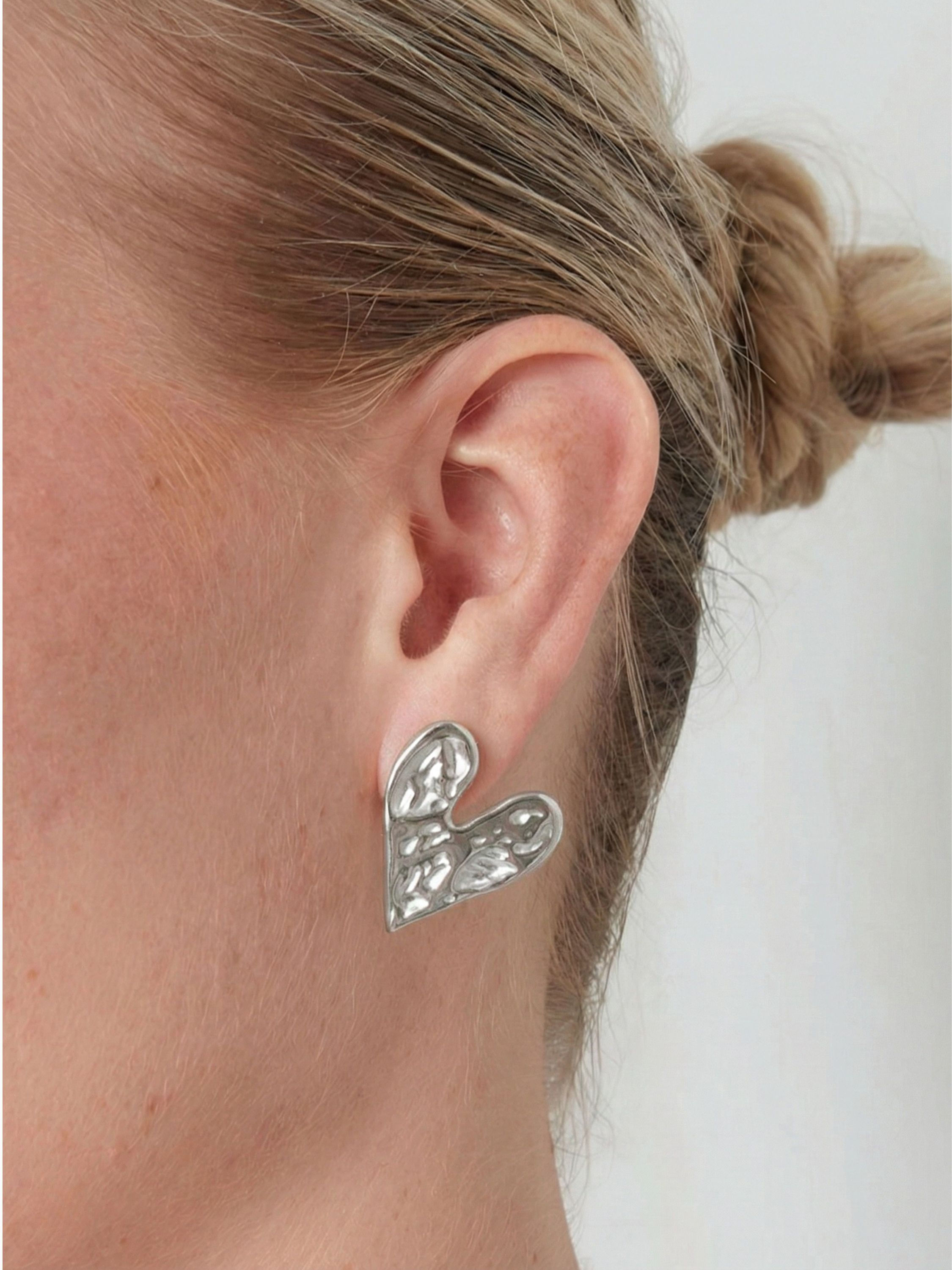 Die silberne Variante der Seloria Herz-Ohrringe am Ohr – zeitloser, architektonischer Edelstahlschmuck für 2026.