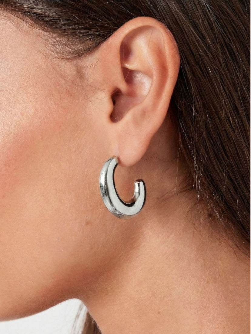 Detailansicht der silbernen Fabiola Ohrringe am Ohr getragen – modernes C-Curve Statement für elegante Looks.