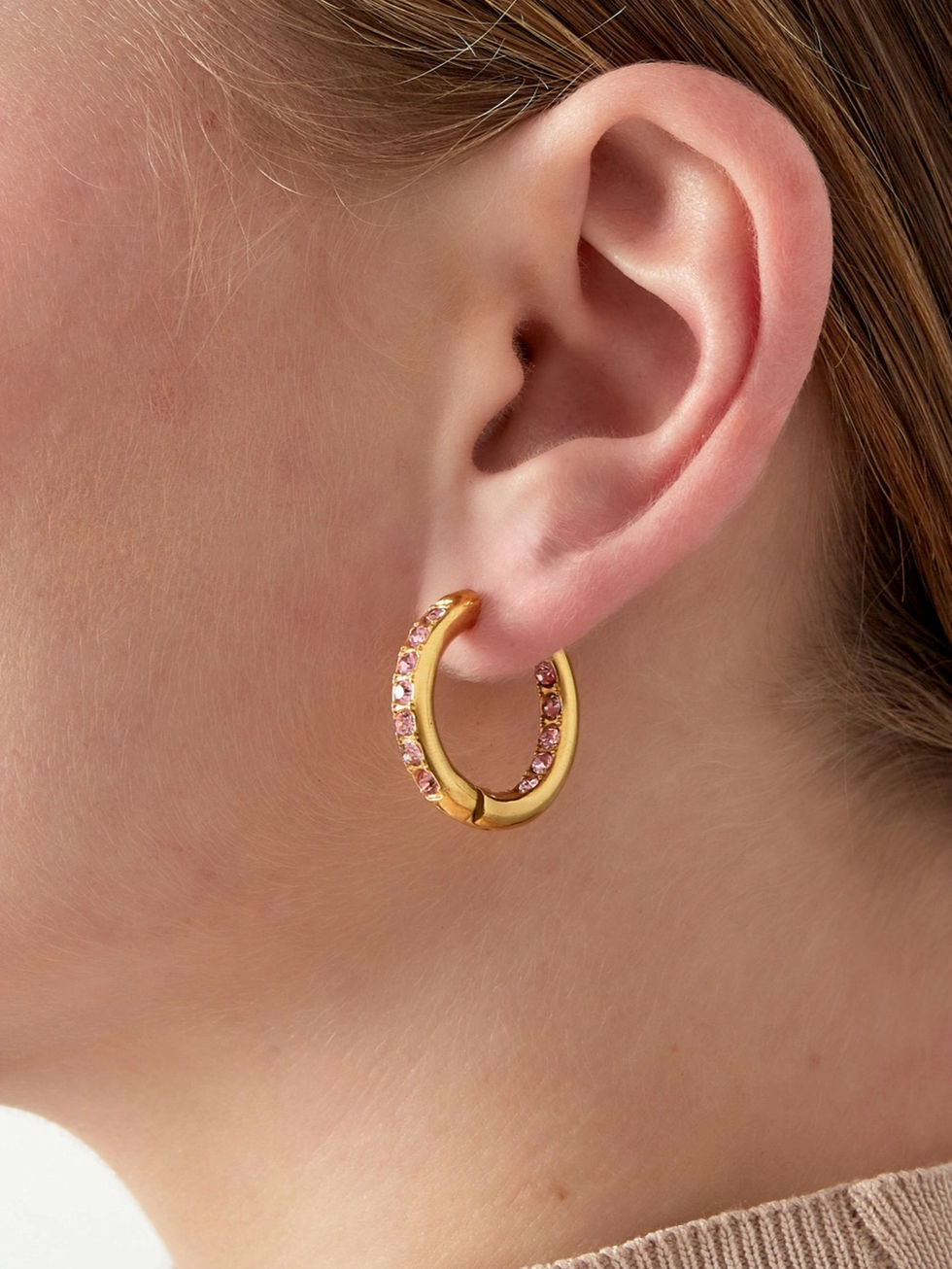 Kleine goldene Creolen mit rosa Steinen am Ohr getragen – eleganter Schmuck-Look.