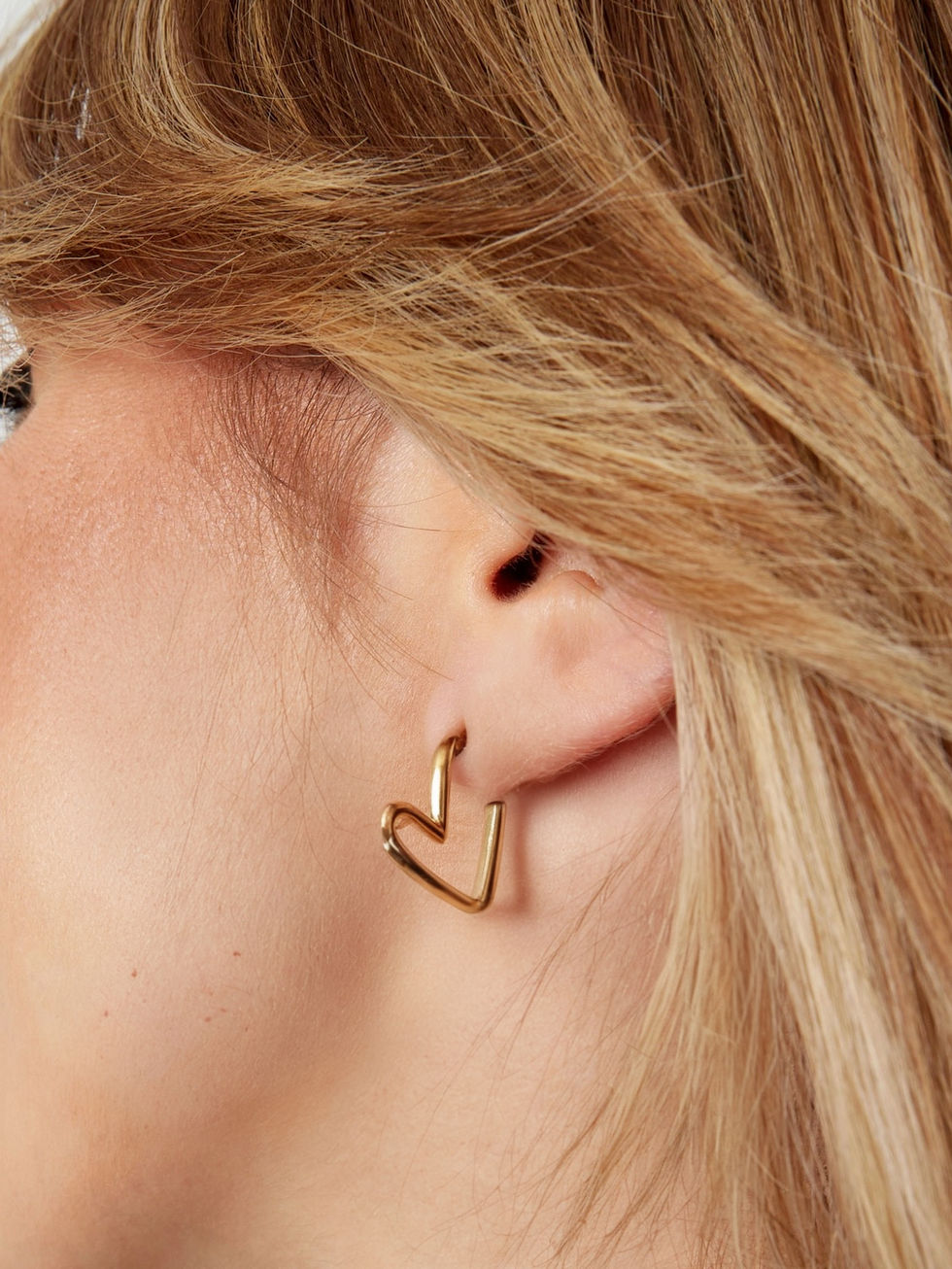 Detailansicht der goldenen Thaloa Herzohrringe am Ohr getragen – modernes minimalistisches Design für elegante Looks.