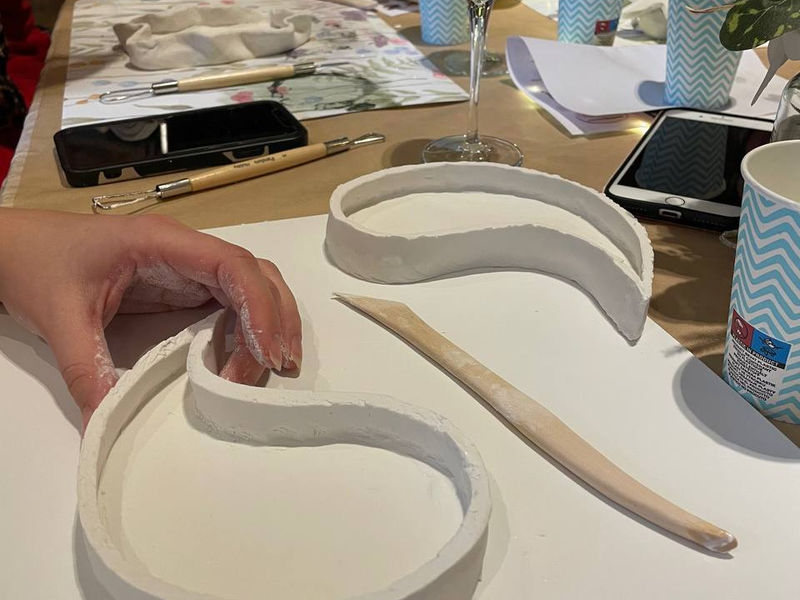 Hands shaping air-dry clay next to a glass of wine