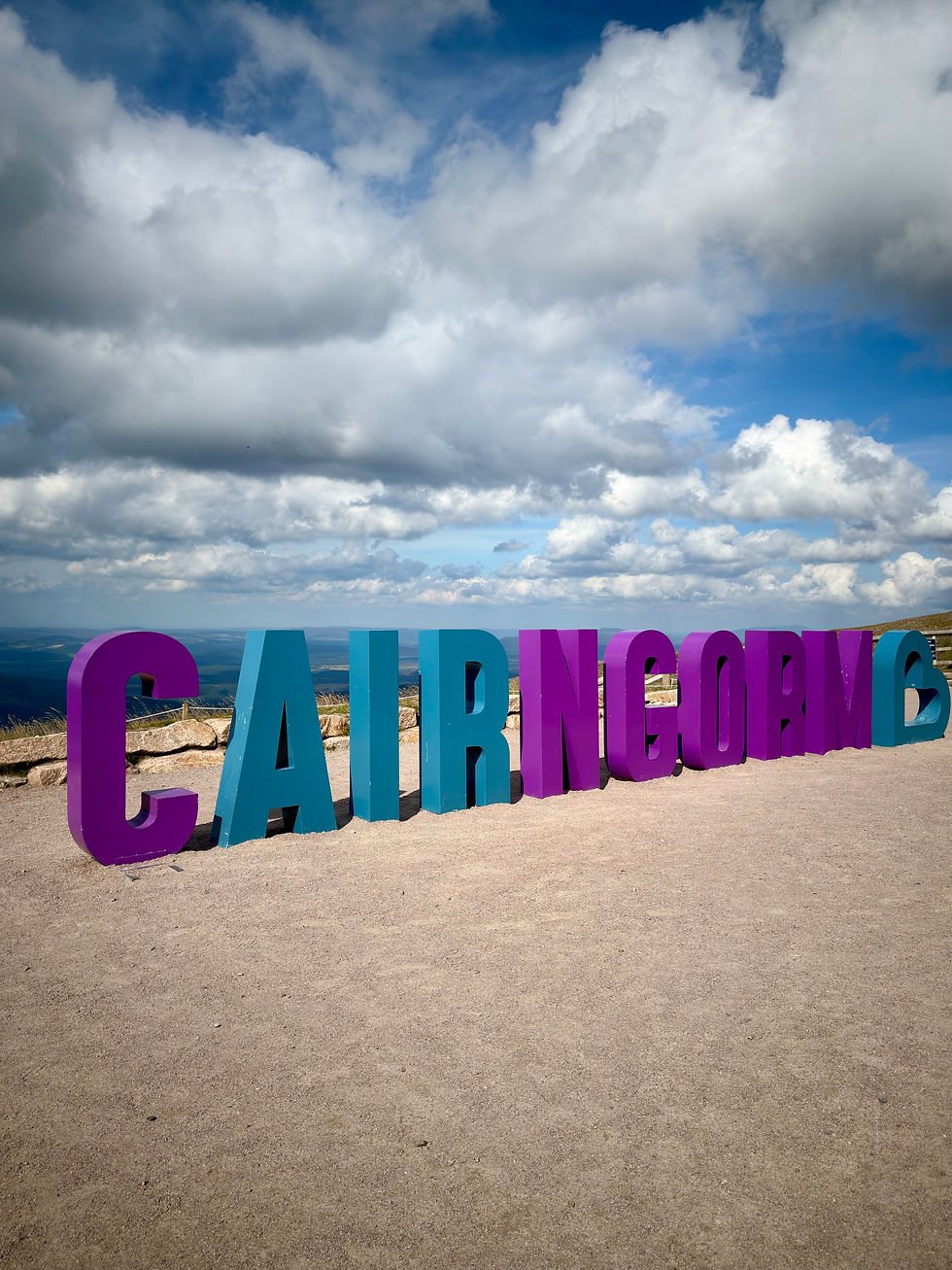 Colorful CAIRNGORMS letters at a windy mountain overlook under dramatic clouds and blue sky