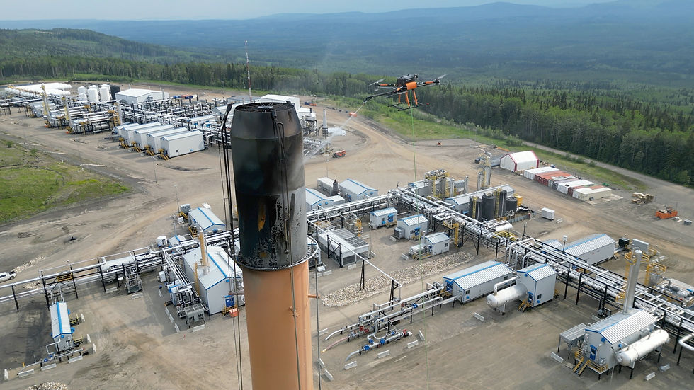 Wide landscape aerial view of an industrial facility with a drone operating near a tall stack