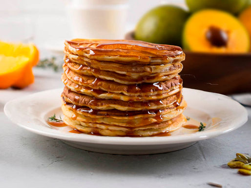 Stack of fluffy lucuma pancakes drizzled with chancaca honey and topped with banana slices — a healthy Andean breakfast made with lucuma flour.