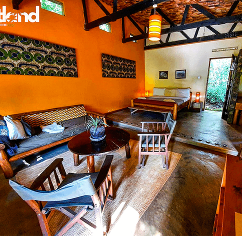 Vibrant orange safari suite with African print wall art, wooden furniture, sofa seating area and double bed at a Uganda lodge