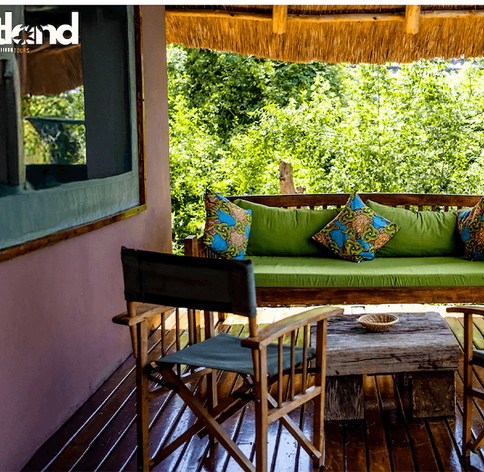 Covered wooden veranda with green sofa and African print cushions overlooking lush forest at a Uganda safari lodge