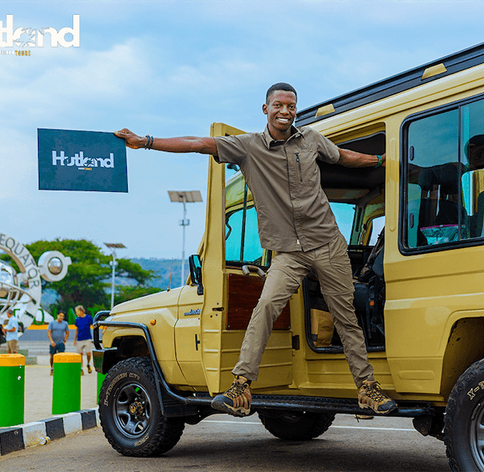 Hutland Tours guide enthusiastically holding a Hutland Tours sign while hanging from a 4x4 Safari Landcruiser at the Uganda Equator monument
