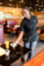 Smiling Keke's Breakfast Cafe server in branded uniform setting jam and butter at a table with coffee and orange juice