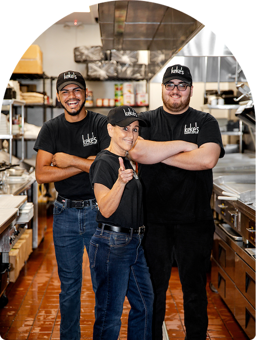 Three Keke's Breakfast Cafe team members in branded shirts and hats posing confidently in the kitchen