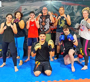 Turma animada de Muay Thai na Academia Krusher Fit, praticando técnicas de autodefesa e condicionamento físico.