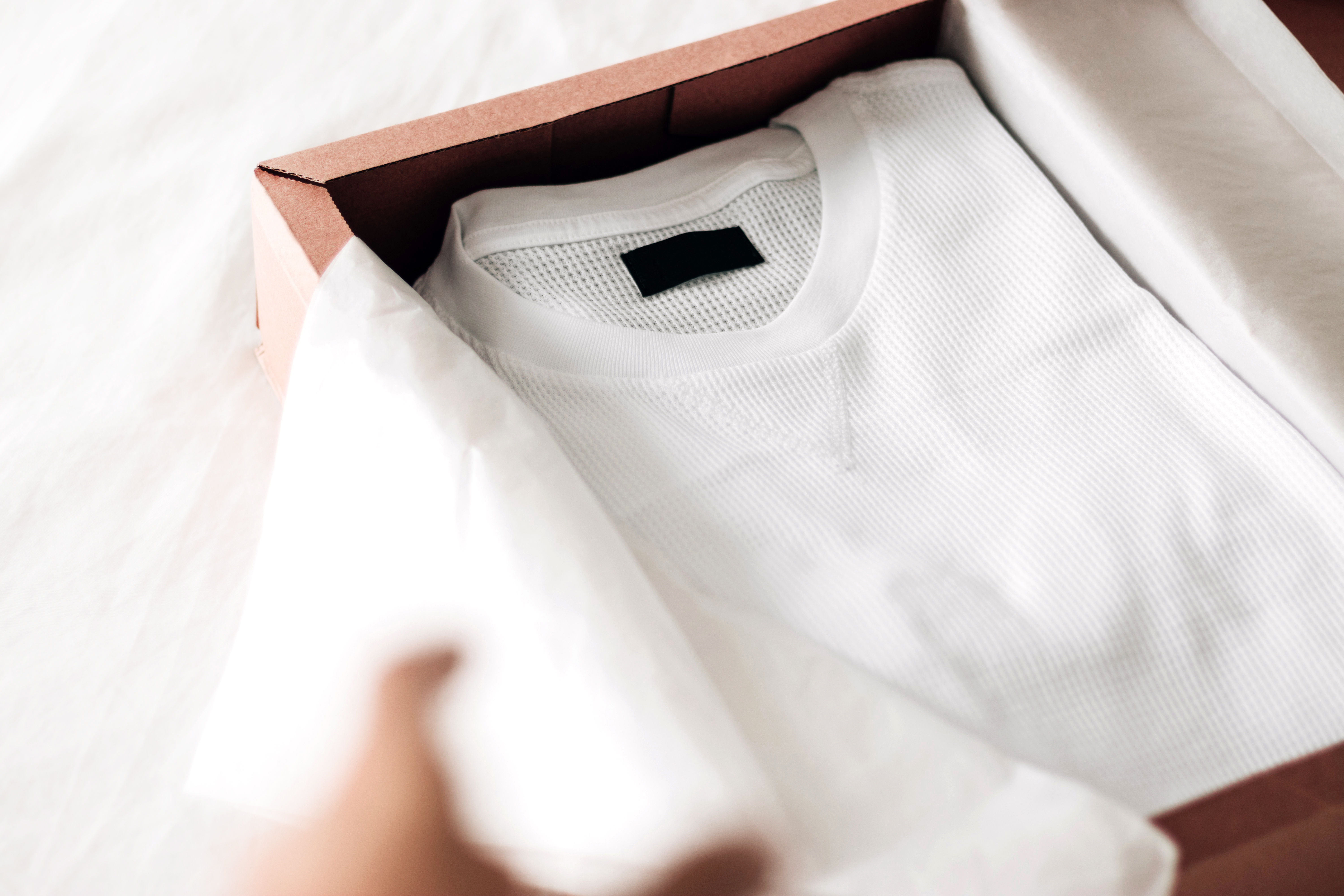 Person excitedly unwrapping a present containing a white crewneck shirt