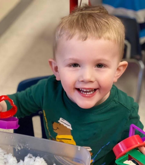 Toddler playing with play sand and smiling at camera