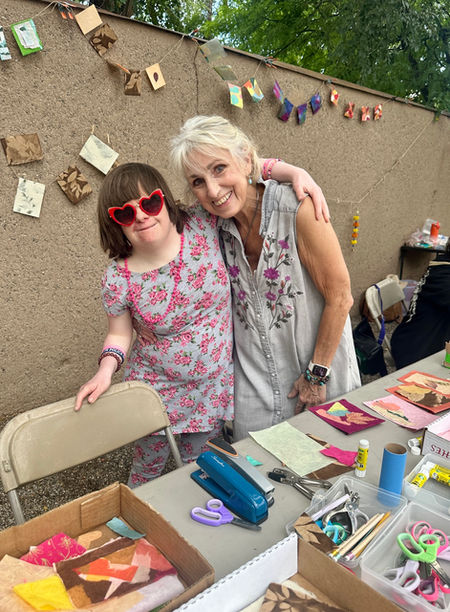 Two women smiling at an outdoor craft table.