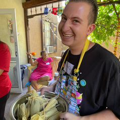 Smiling young man holding a large bowl of tamales outdoors.