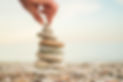 A hand is reaching for a stack of rocks, which are arranged in a pyramid shape. Concept of