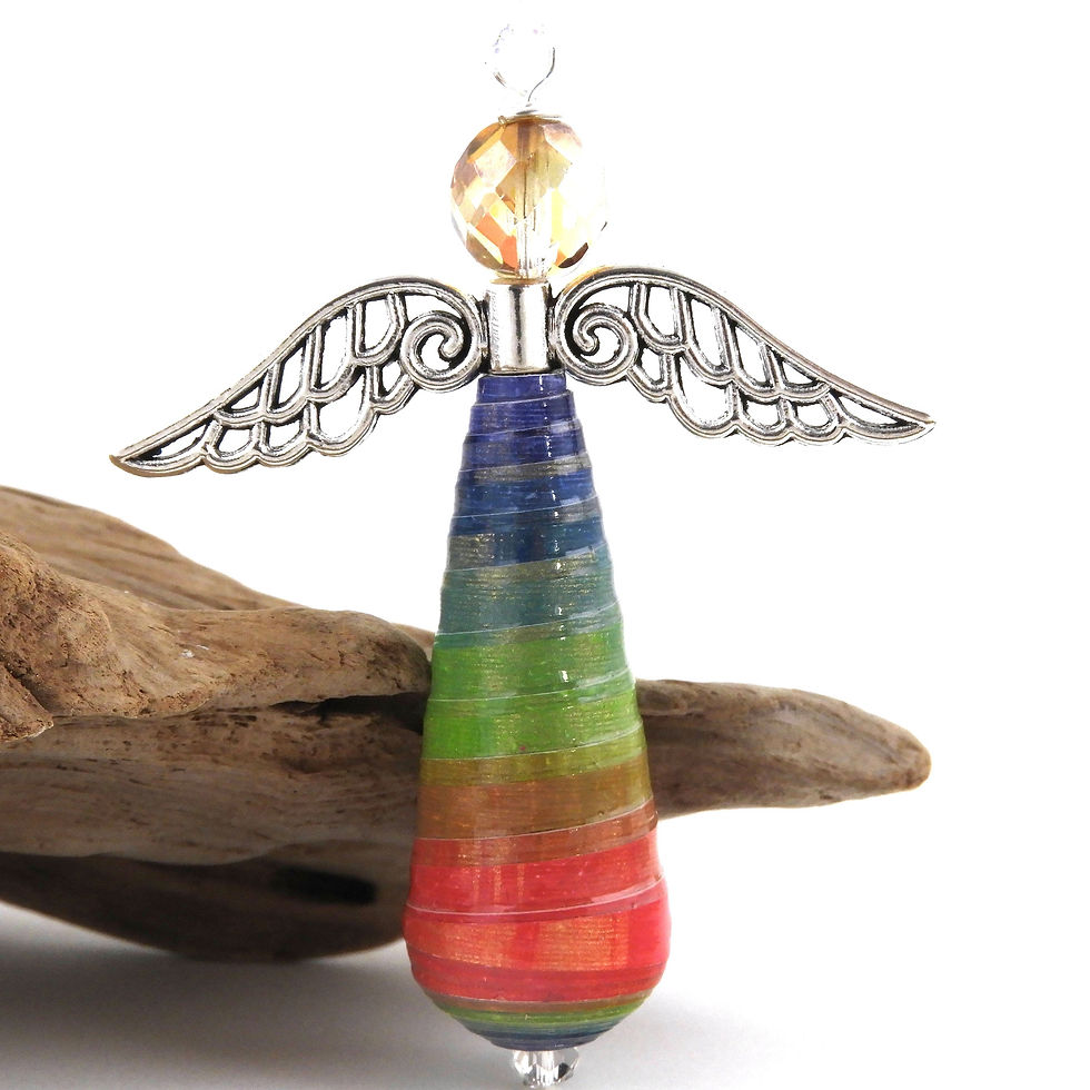 Blue, green, and red paper bead angel ornament standing in front of driftwood.