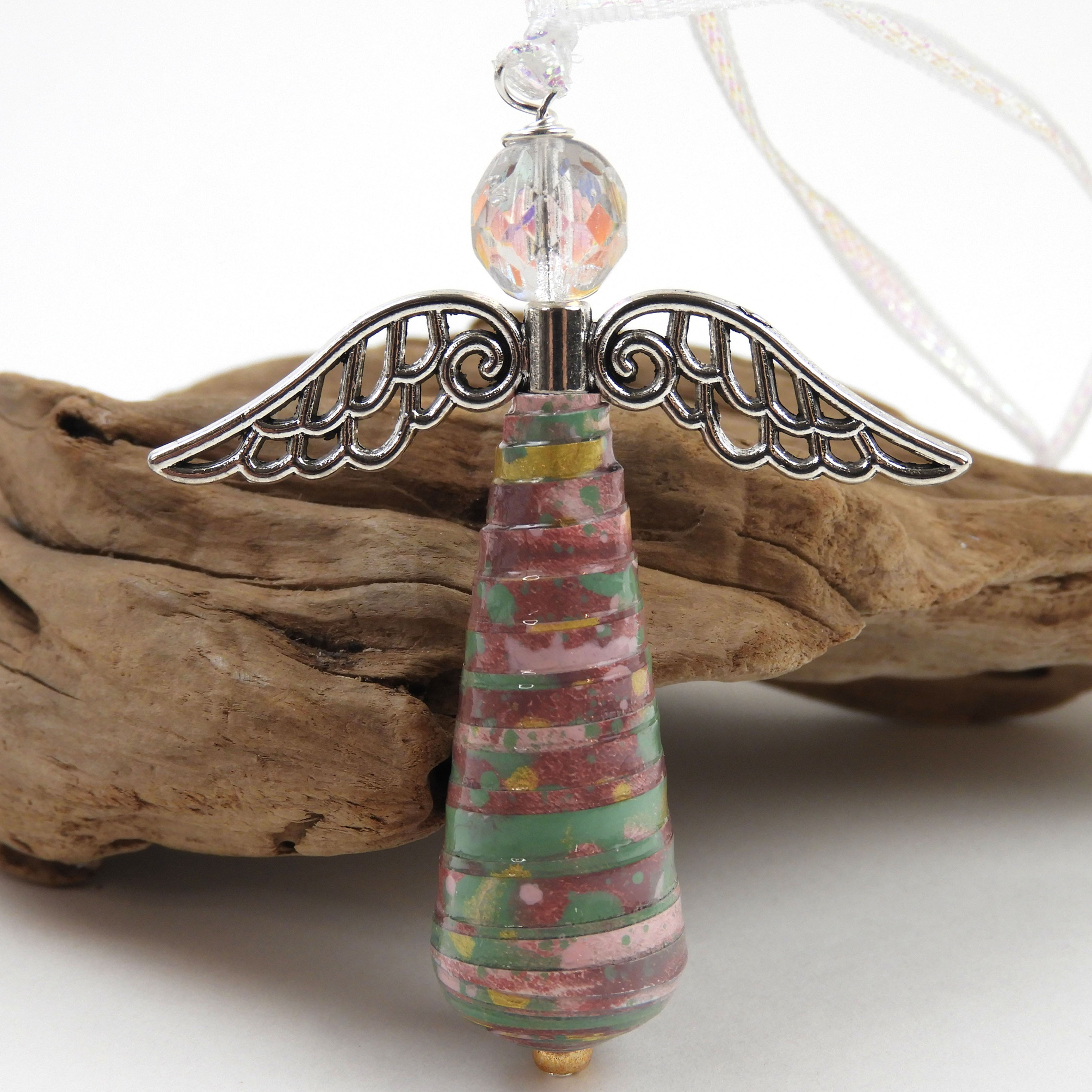 Purple, teal, and gold paper bead angel ornament standing in front of a piece of driftwood.