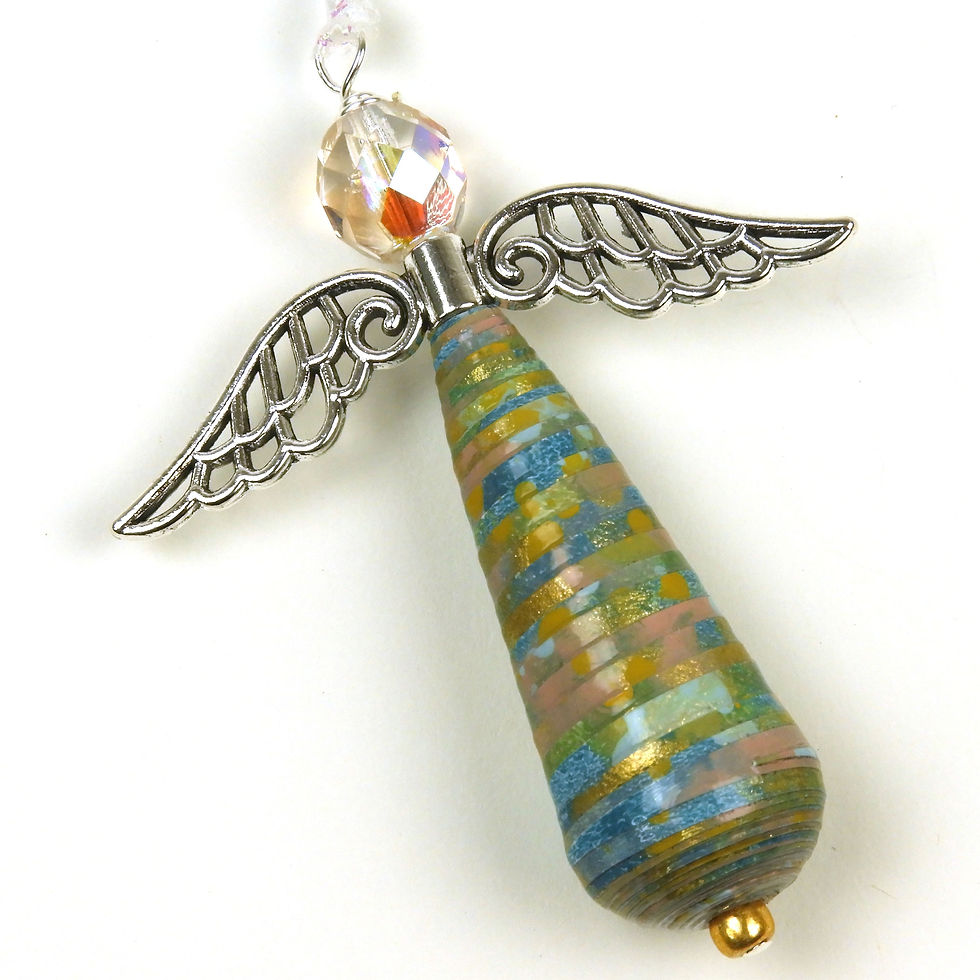 Green, teal, pink, gold, and blue paper bead angel ornament laying diagonally on a white background.