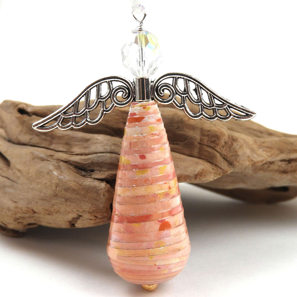 Shades of pink and gold paper bead angel ornament standing in front of driftwood.