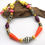 Thumbnail: Yellow, pink, coral, purple, gold, black, and white paper bead necklace draped over a piece of driftwood.