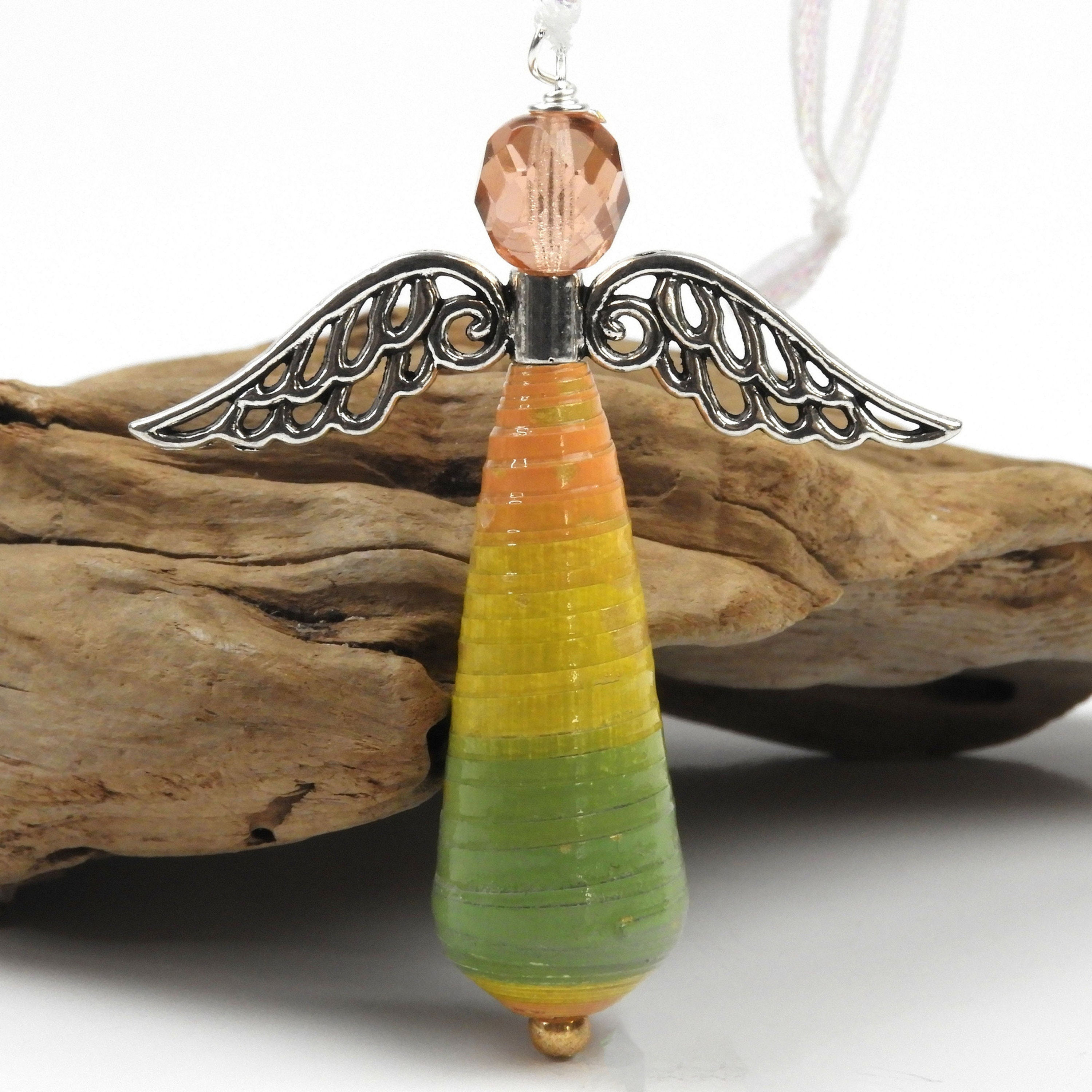 Orange, yellow, and green striped paper bead angel ornament standing in front of driftwood.