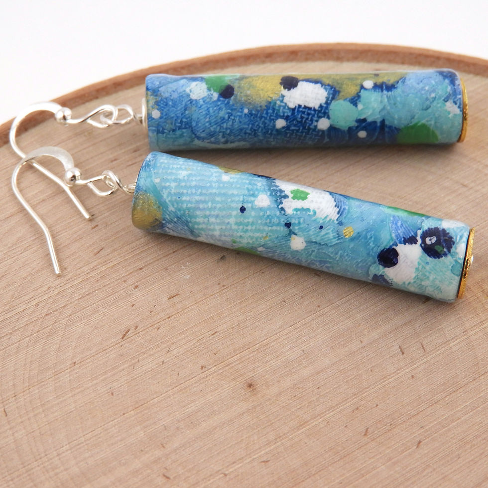 Thumbnail: Blue, white, and gold abstractly painted paper bead earrings on a wood background.