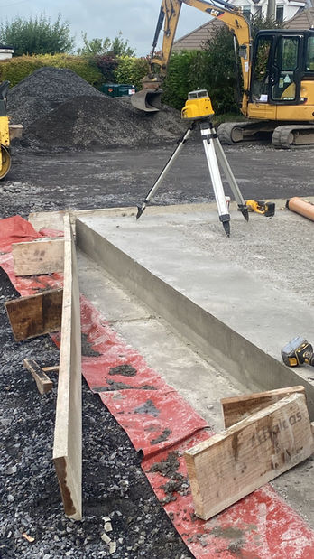 Concrete formwork, laser level, excavator on site.