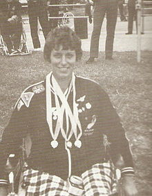 black and white photo of Eve Rimmer in her wheelchair with medals around her neck. She is smiling