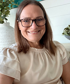 Smiling woman with glasses in a beige ruffled top.