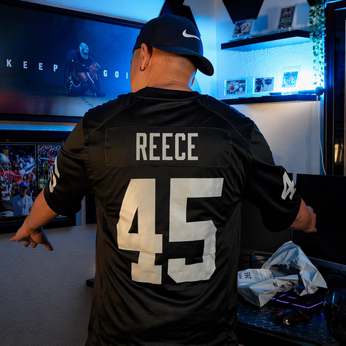 A man in a custom black jersey with the name "Reece" and the number "45" on the back. His back is turned toward us so we see his jersey. In front of him, he has a custom room with a lebron scoring champ poster, a computer, and other knick knacks.