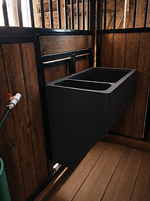 Custom horse stall feed system with black metal troughs and warm wood panels, showcasing premium Canadian-made stable design and functional equestrian facility craftmanship