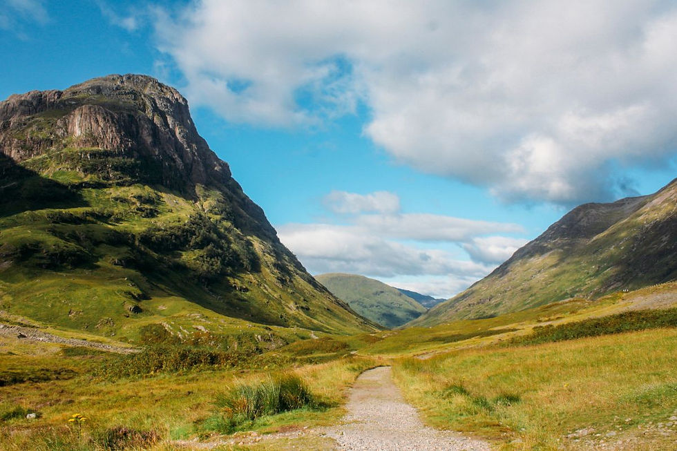 A lush valley with a winding path, flanked by towering green mountains under a bright blue sky with scattered clouds. Peaceful mood.