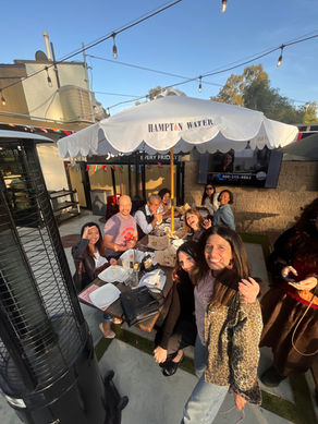 Group of People around a table with an umbrella smiling
