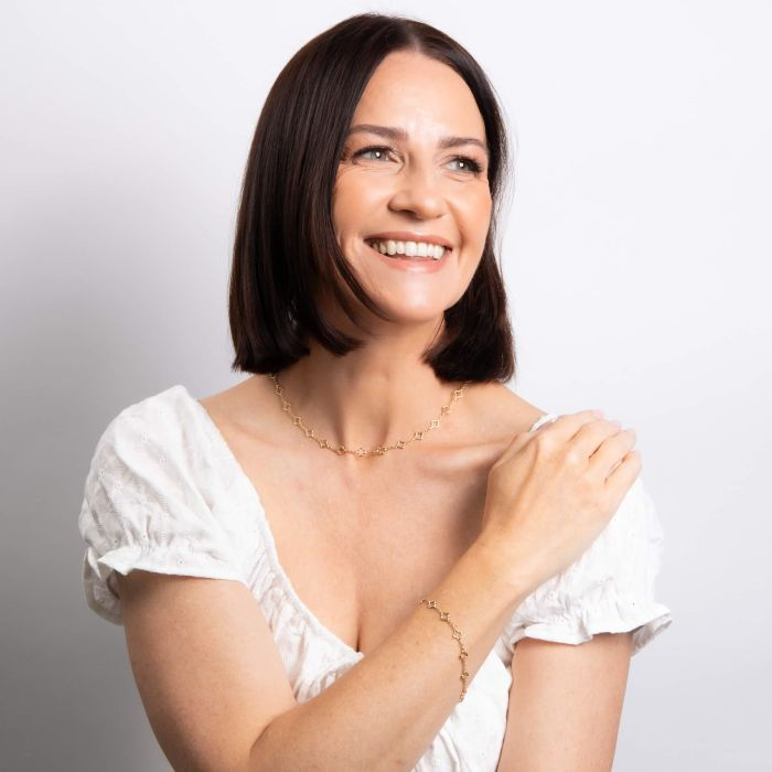 Thumbnail: Smiling woman holding arm, wearing white top, and Quatrefoil Station Bracelet. Léonce & Co.