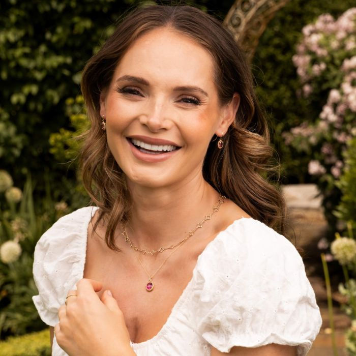 Thumbnail: Smiling woman wears a white dress with Oval Cut Pink Topaz Drop Earrings in garden setting