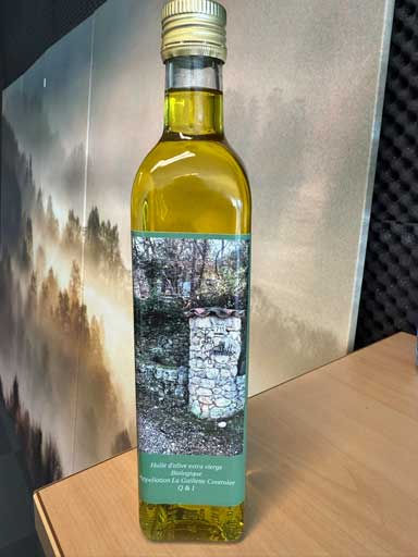 Een fles zelfgemaakte olijfolie staat op een houten tafel.