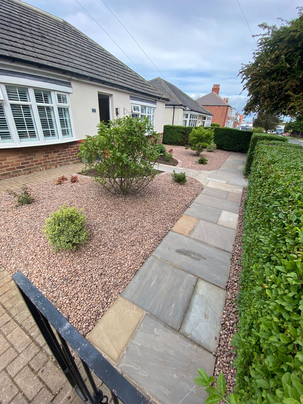 Front garden featuring natural stone paving pathway bordered by decorative gravel, clipped hedging and newly planted ornamental shrubs leading towards the property’s entrance.