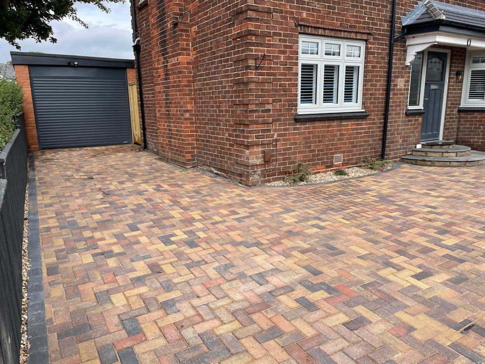 Block paved driveway with warm multi-tone bricks and curved edging leading to a red brick house.
