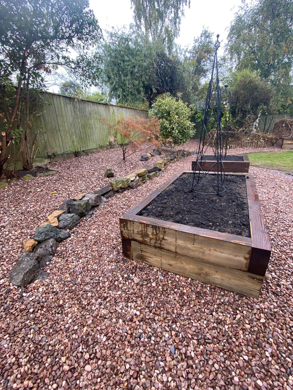 Two timber raised beds with supports in a gravelled area, ready for new planting.