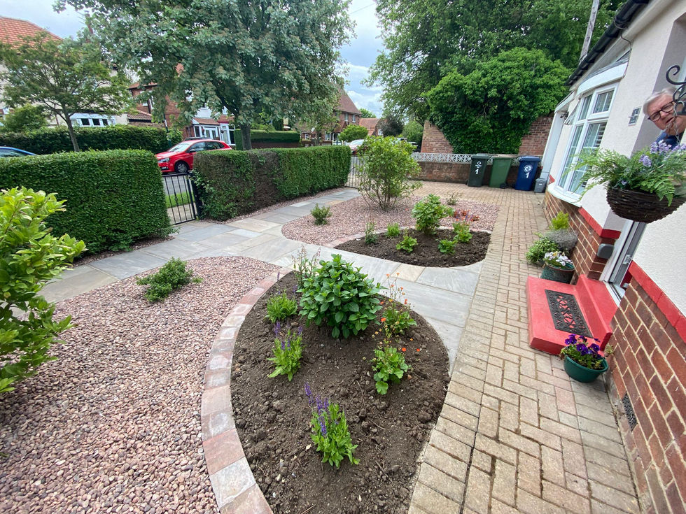 Central natural stone pathway leading to the front gate, framed by curved planting beds containing hydrangeas, flowering perennials and ornamental shrubs.
