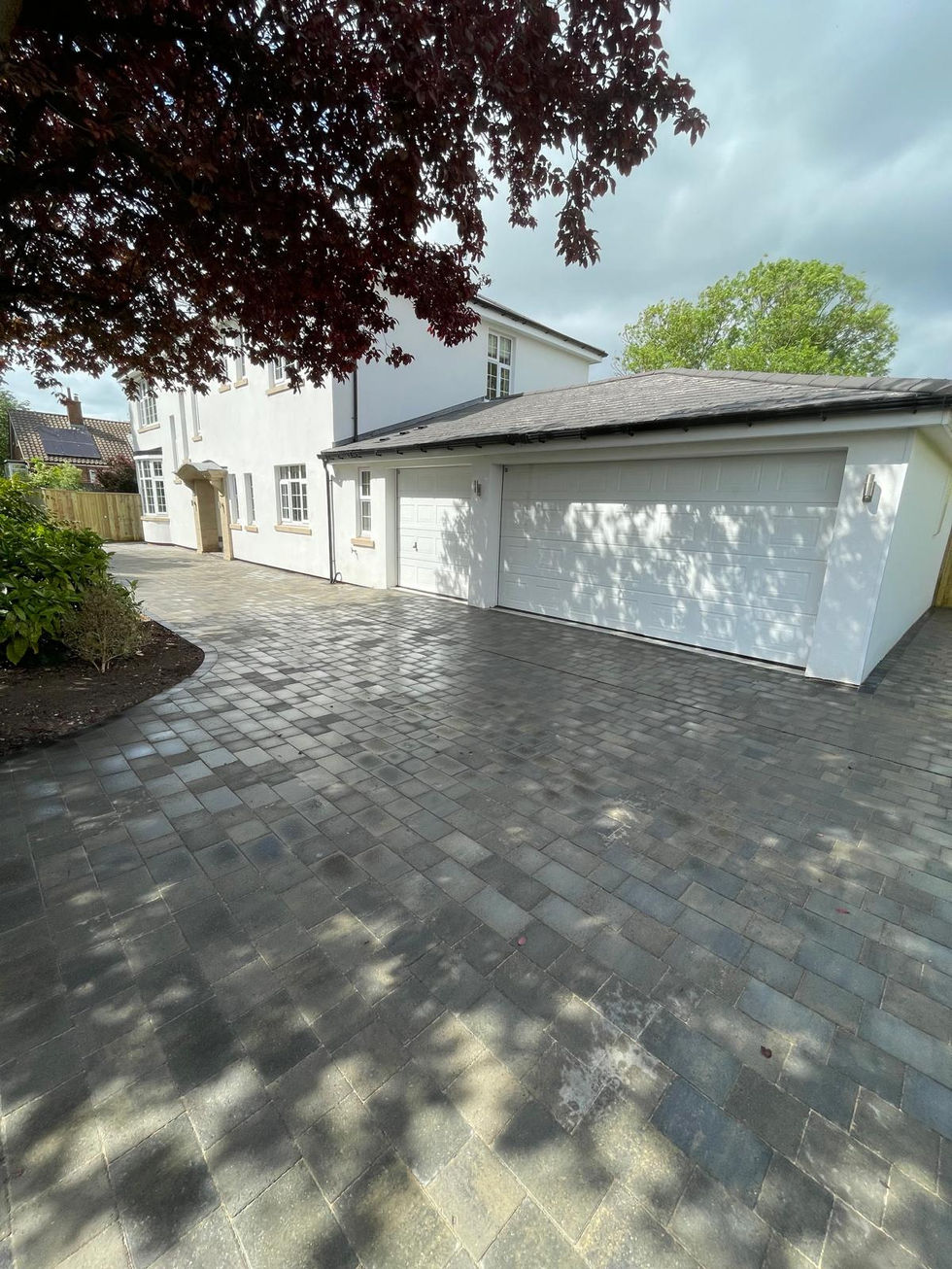 Photographs showing a completed grey block paved driveway and side access at a white detached property. The installation features contemporary paving laid across the front and side of the home, creating a clean, durable and low-maintenance surface that enhances the property’s kerb appeal.