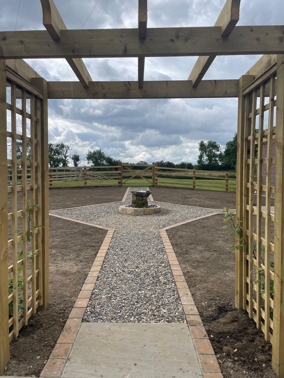 View through pergola framing gravel path and water feature with soil areas either side.
